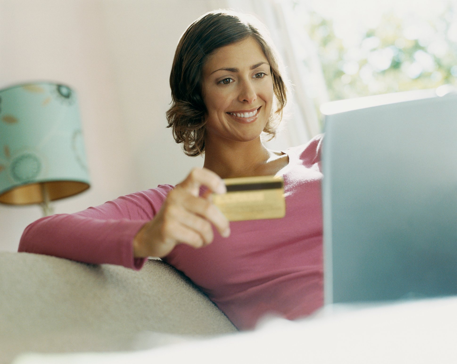 A woman looking at a laptop and smiling while holding a credit card