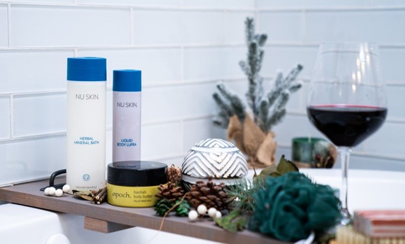 Nu Skin products on a tray over a bath, accompanied by a glass of wine.