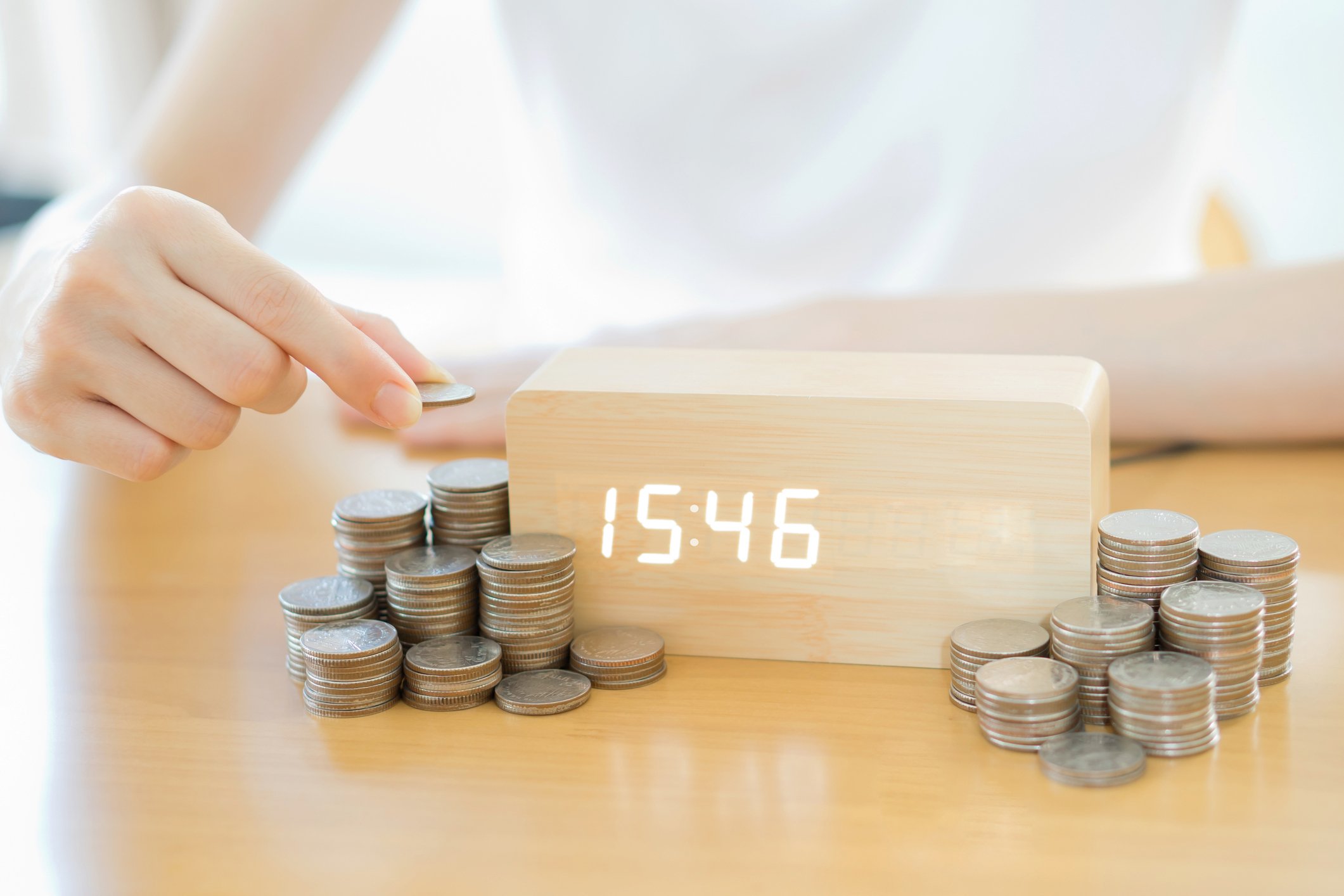 A woman is stacking coins in piles around a modern digital clock.