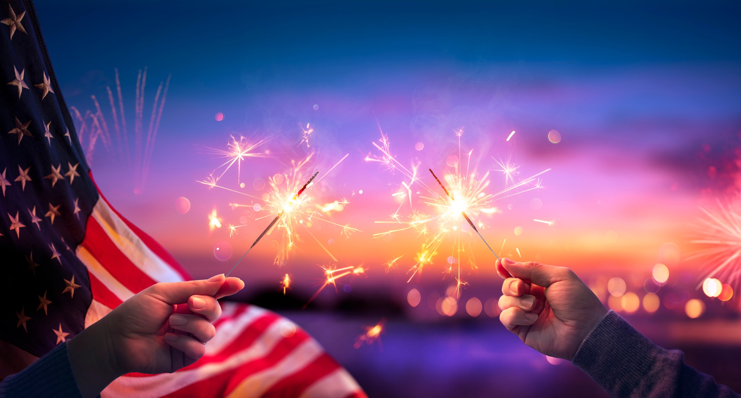 Hands holding sparklers in front of American flag background.