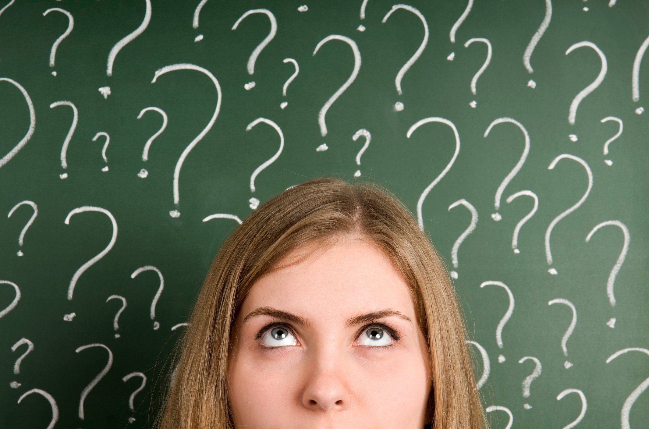 Woman standing in front of a board with dozens of question marks drawn on the board. 