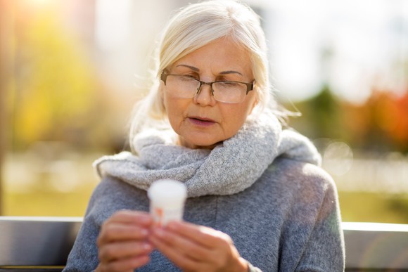 Older woman on bench looking at prescription bottle