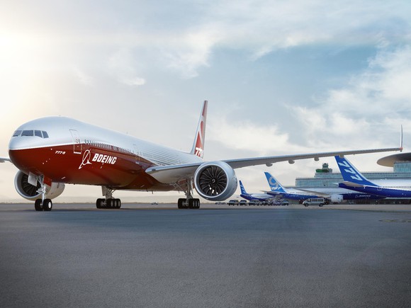 Red and white Boeing aircraft taxiing away from three blue and white Boeing aircraft parked at gates.