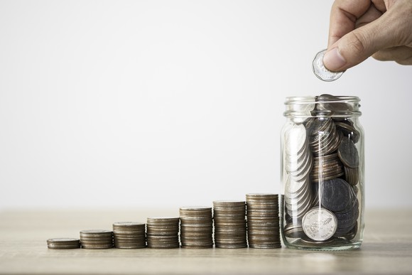 Progressively taller stacks of coins next to a jar full of coins 