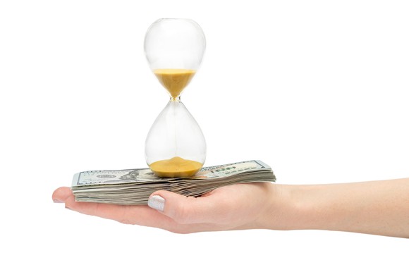 Hand holding hourglass on top of cash