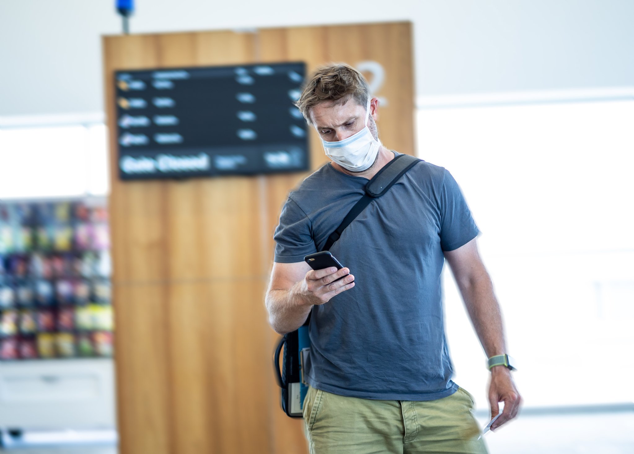A man looks at his phone while wearing a face mask in an airport.