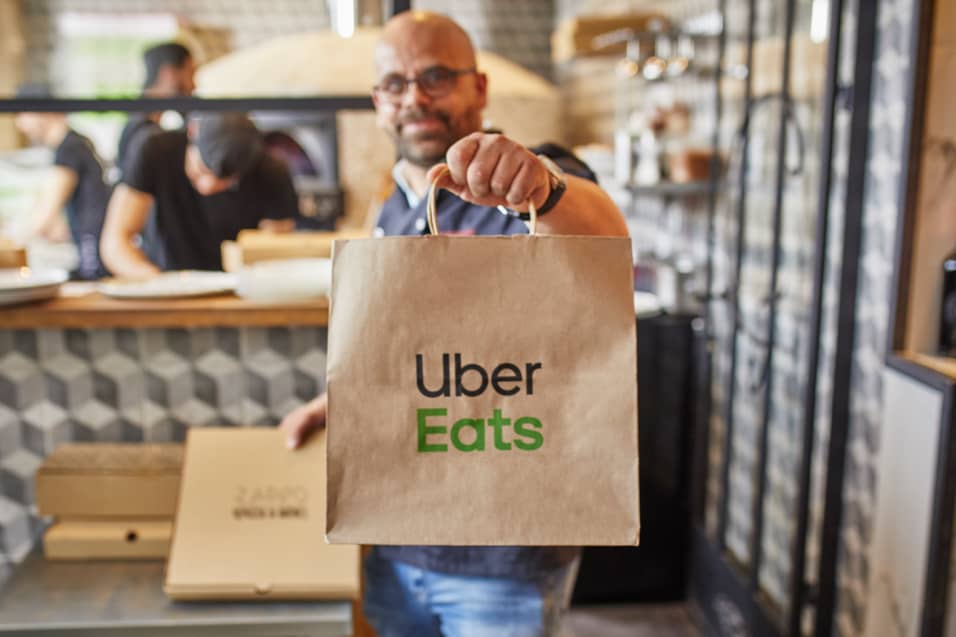Man holding up an Uber Eats bag in restaurant