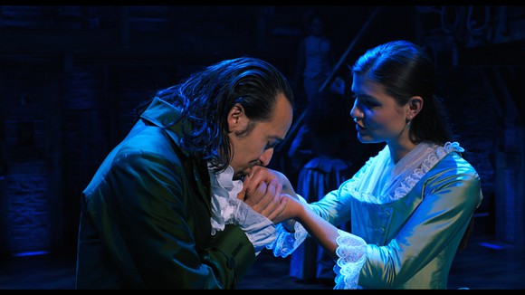 A man in colonial dress affectionately kissing a woman's hand. 