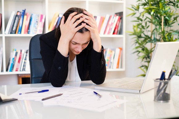 Woman holding her head in her hands at desk.