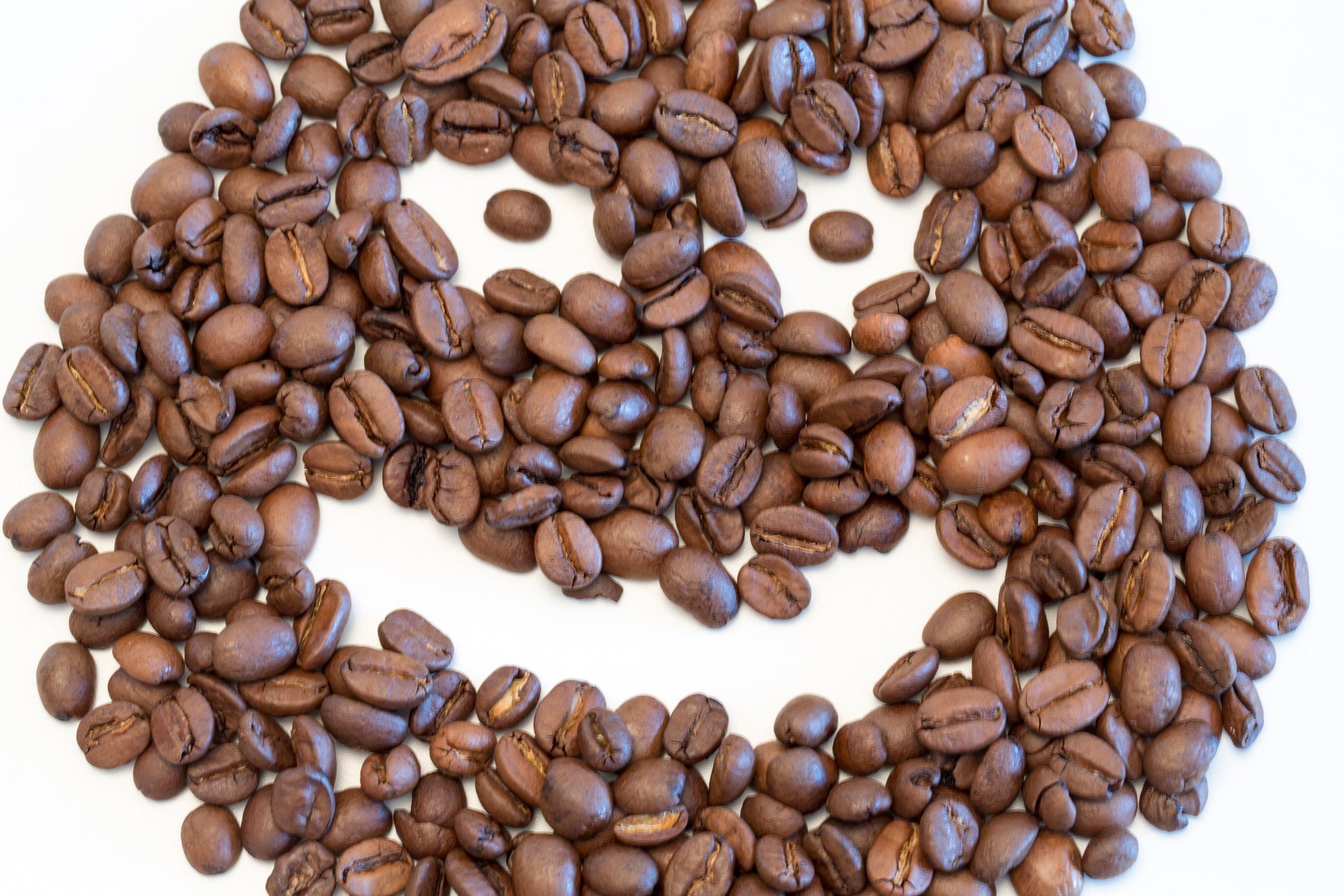 A scary looking face is made with a pile of coffee beans against a white background. 