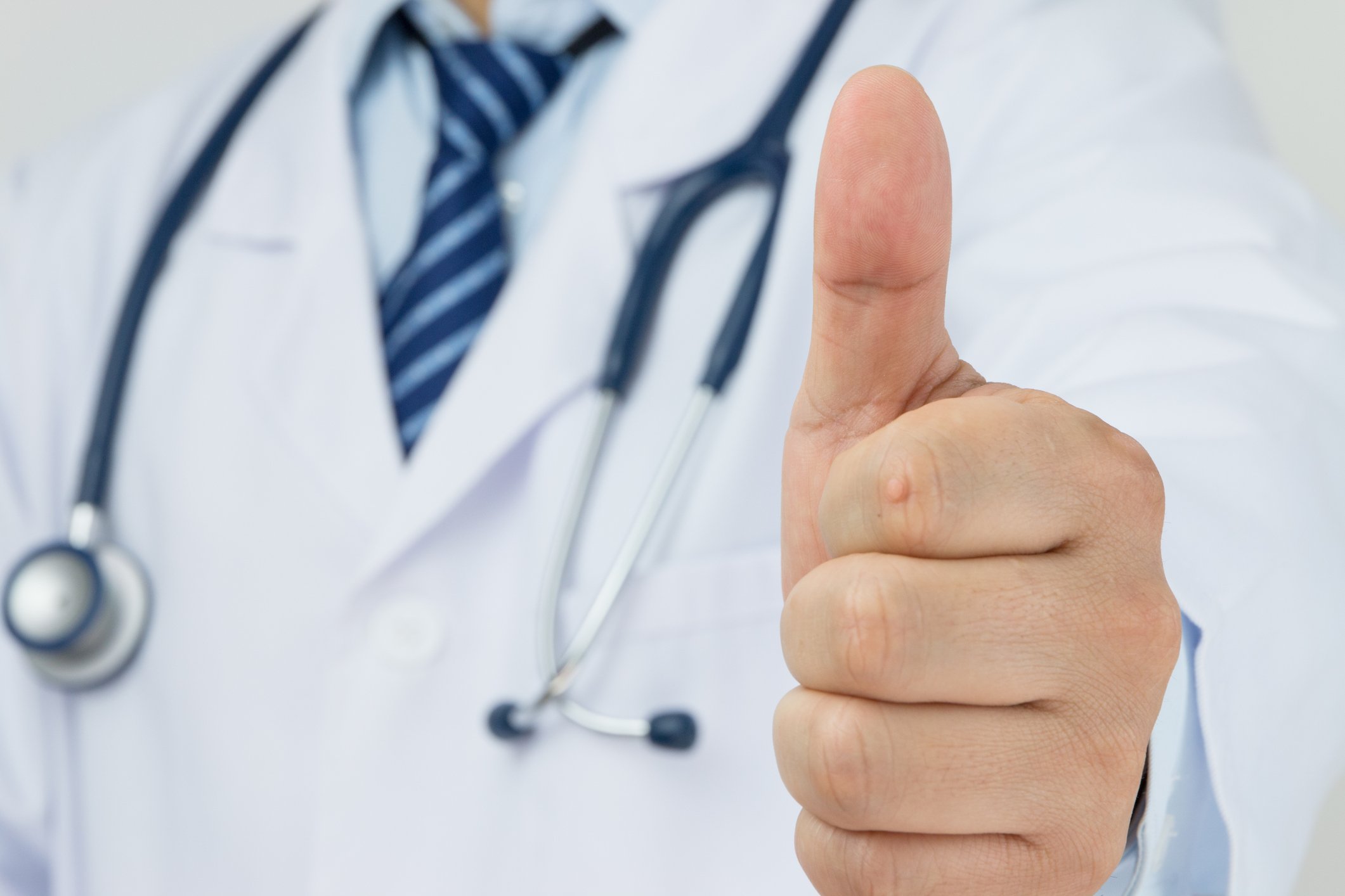 A physician with a stethoscope around his neck giving the thumbs-up sign.