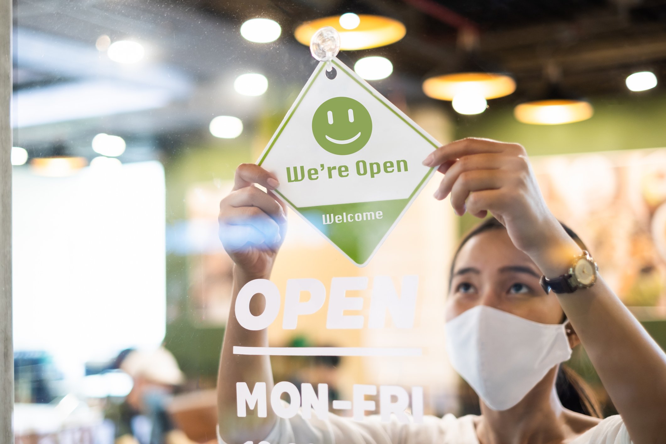 Restaurant owner wearing a mask flips "open" sign on window.