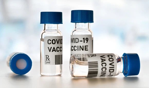 Four blue-capped vials labeled COVID-19 vaccine on a table.