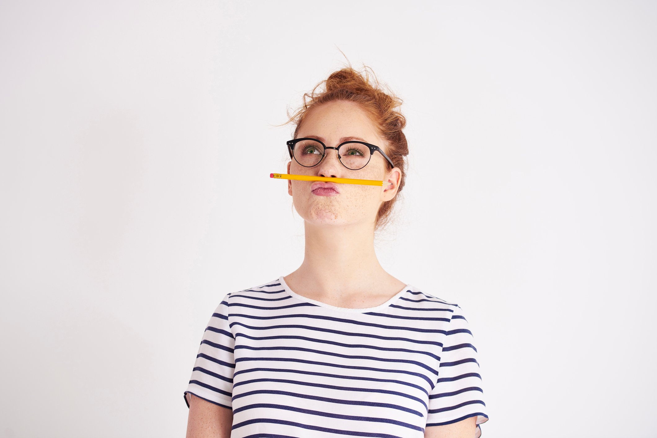 Woman holding pencil between her nose and upper lip.