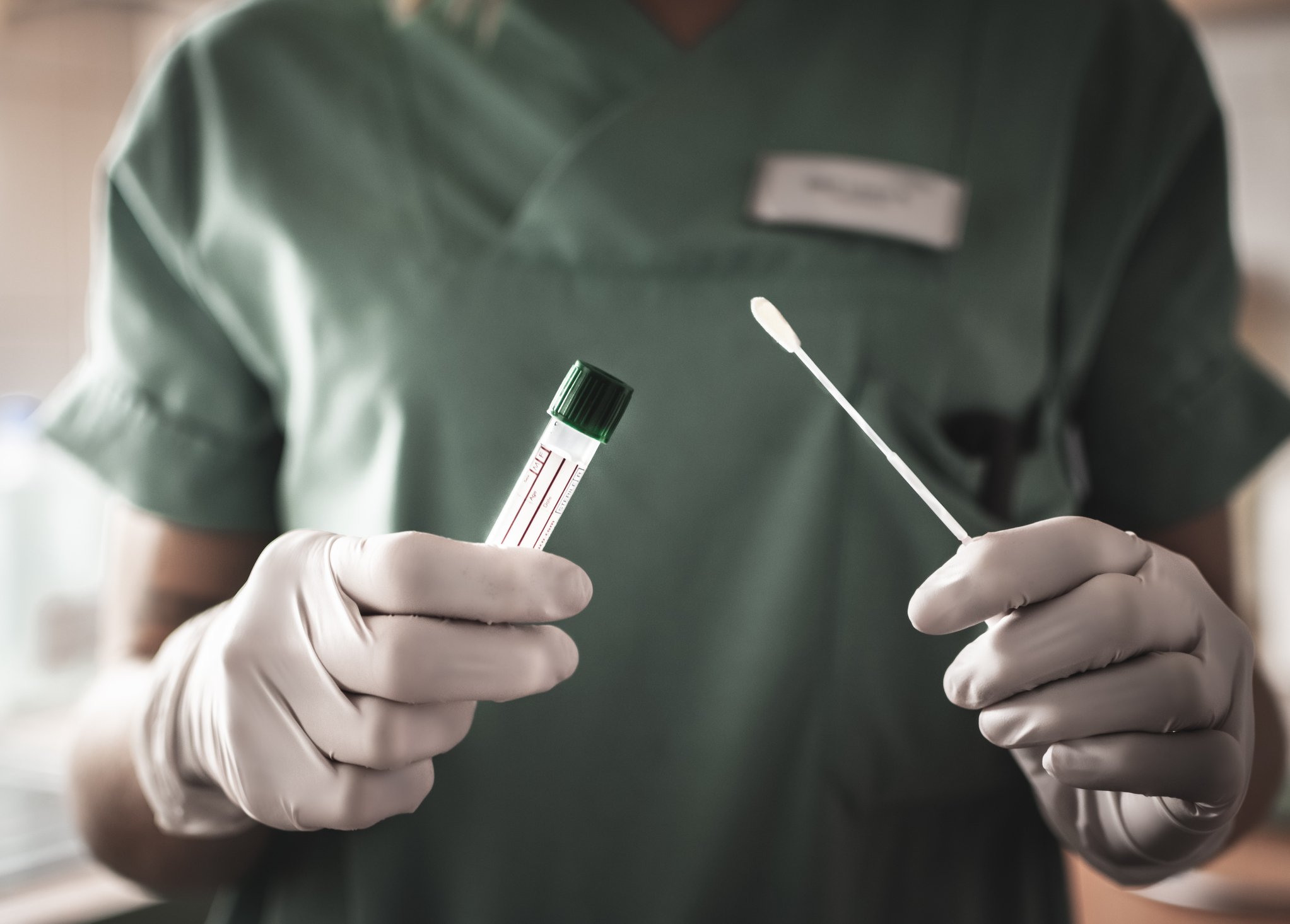 A medical professional holds a COVID-19 test tube and testing swab.