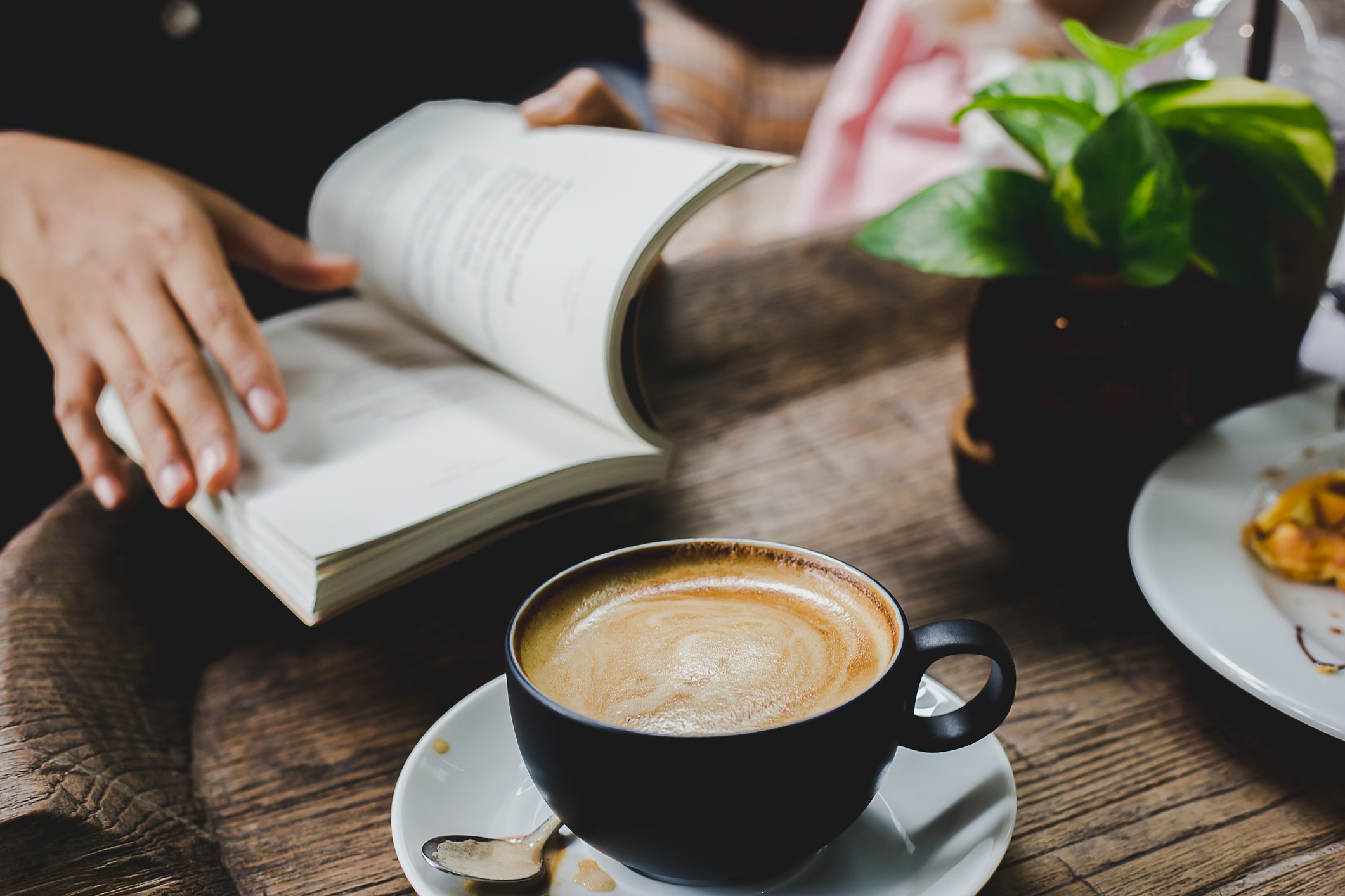 Person reading book with a cup of coffee beside them on table