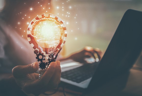 A person holding a light bulb with gears and a brain inside.