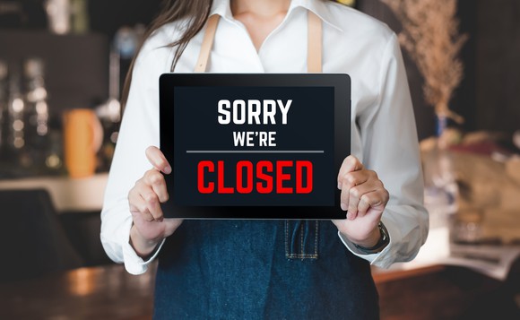 A restaurant worker holds up a sign saying Sorry we're closed.