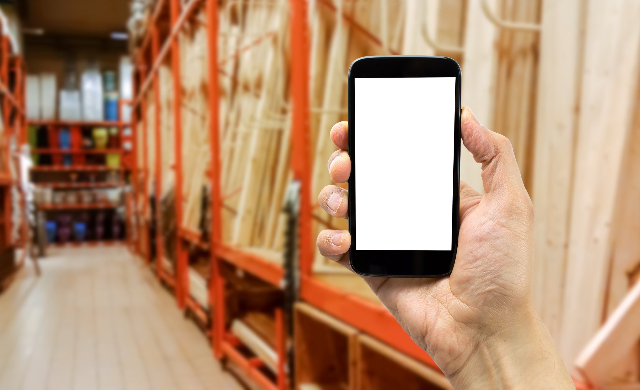 A hand holding up a smartphone in the lumber section of a home-improvement store