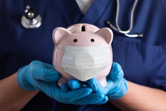 A doctor holds a masked piggy bank in gloved hands.