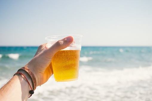 A hand holding a cup of beer on a beach