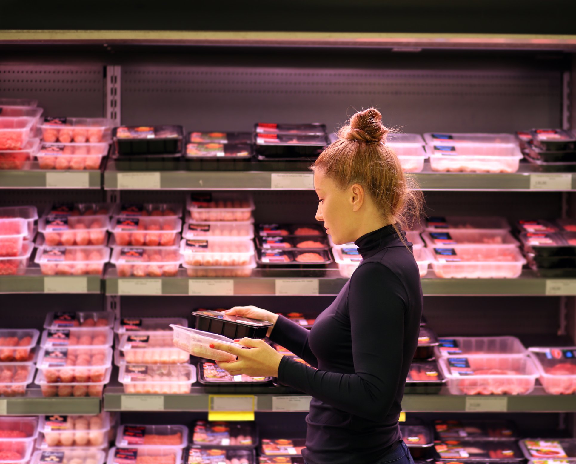 A woman shopping in the meat section of the grocery store.