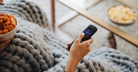 A hand holding a Roku remote.