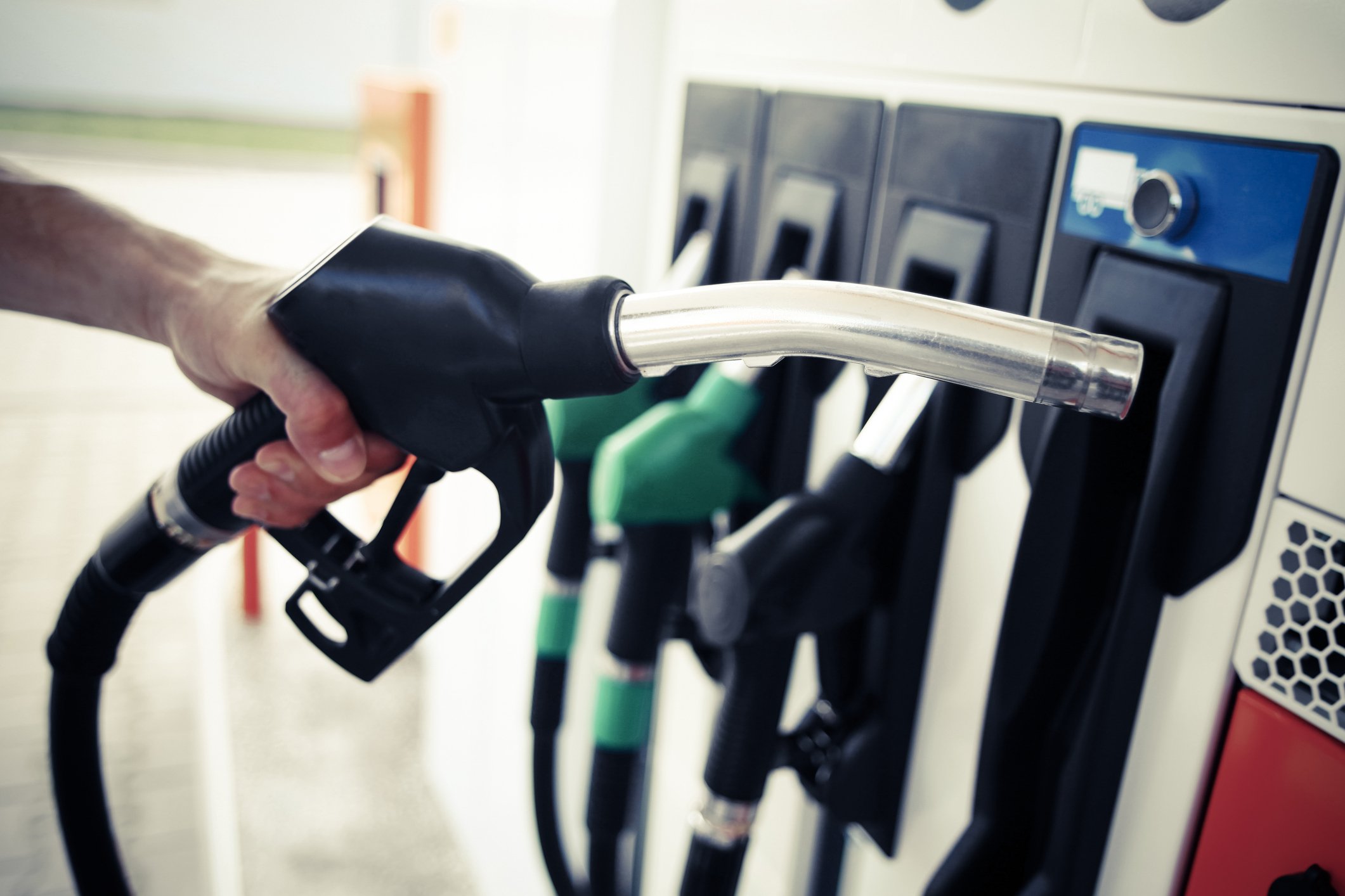 A man's hand holds a gas pump at a filling station.