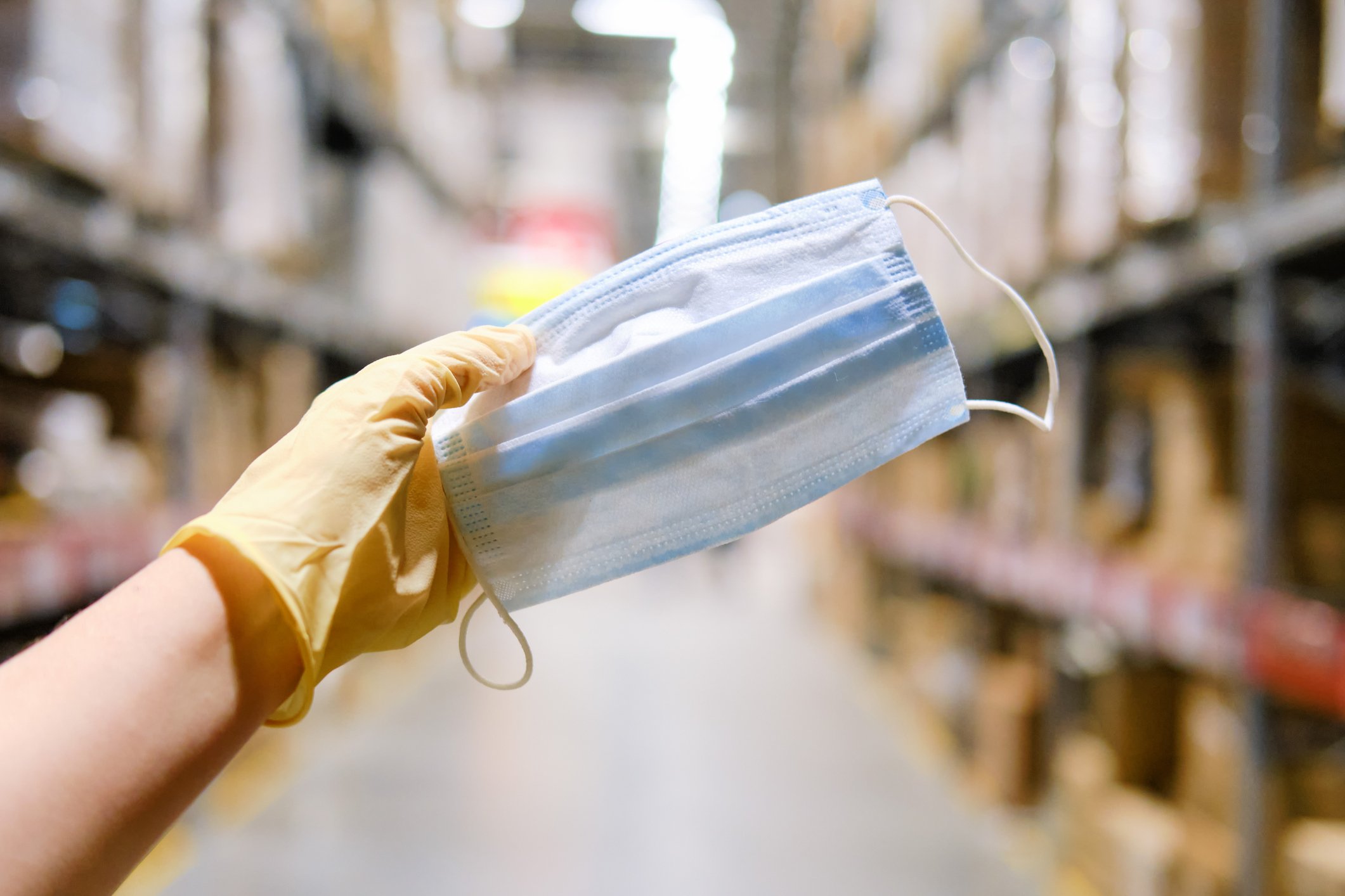 A gloved hand holding up a facemask for shopping in a warehouse store.