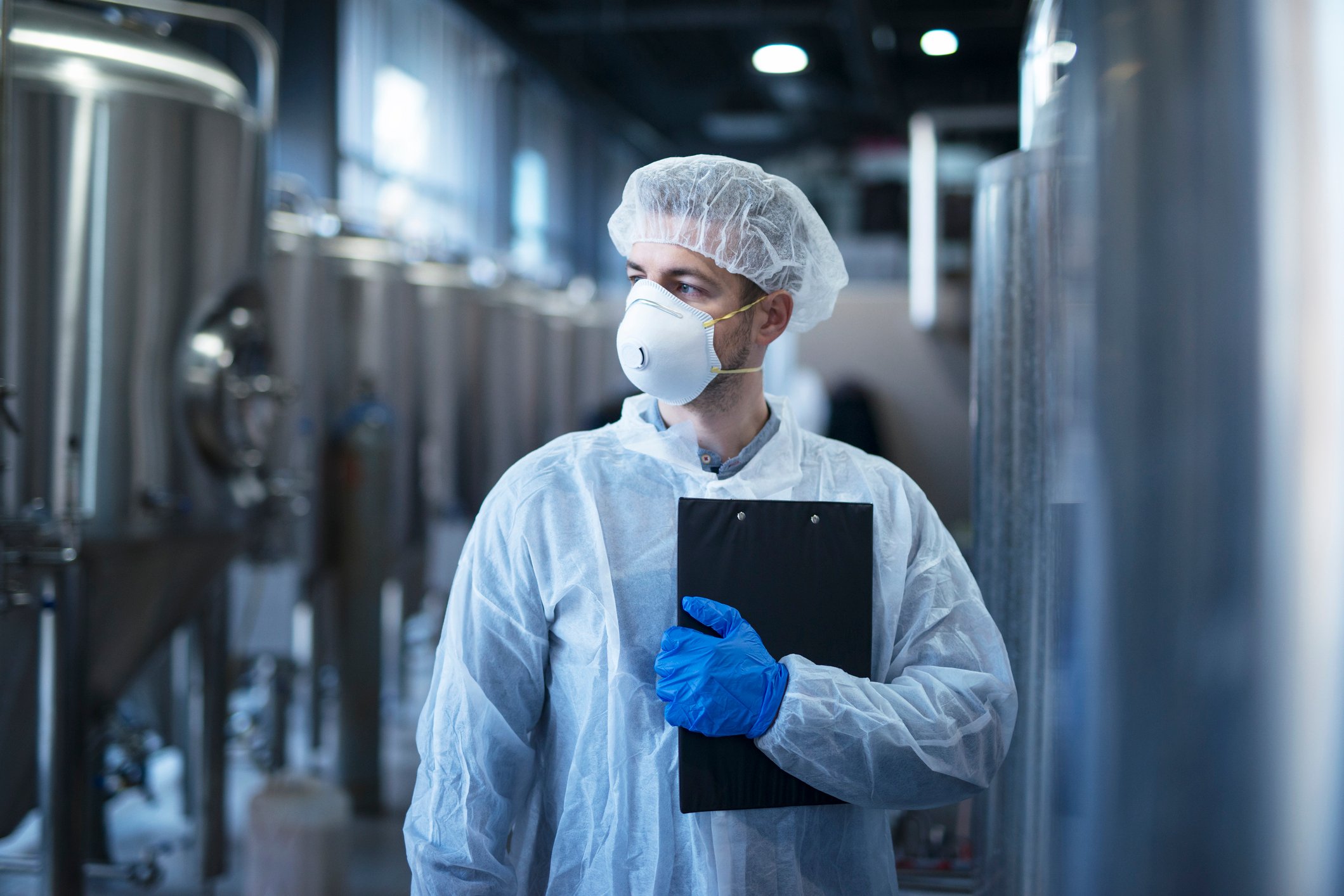 A person in coveralls, mask, and hood near food equipment machinery.