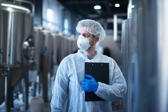 A person in coveralls, mask, and hood near food equipment machinery.