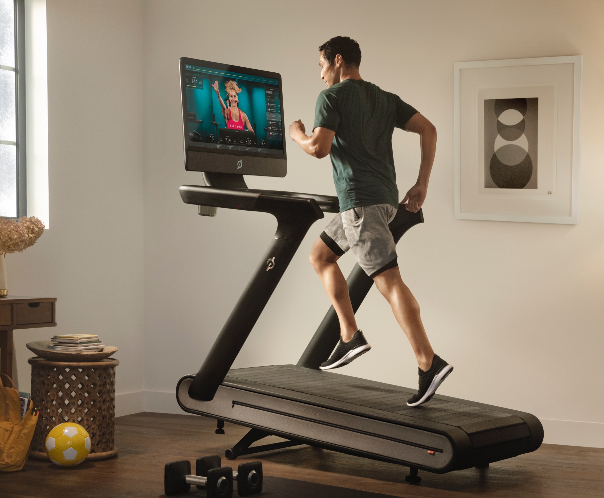 A man is walking on a Peloton treadmill while watching a fitness class. 