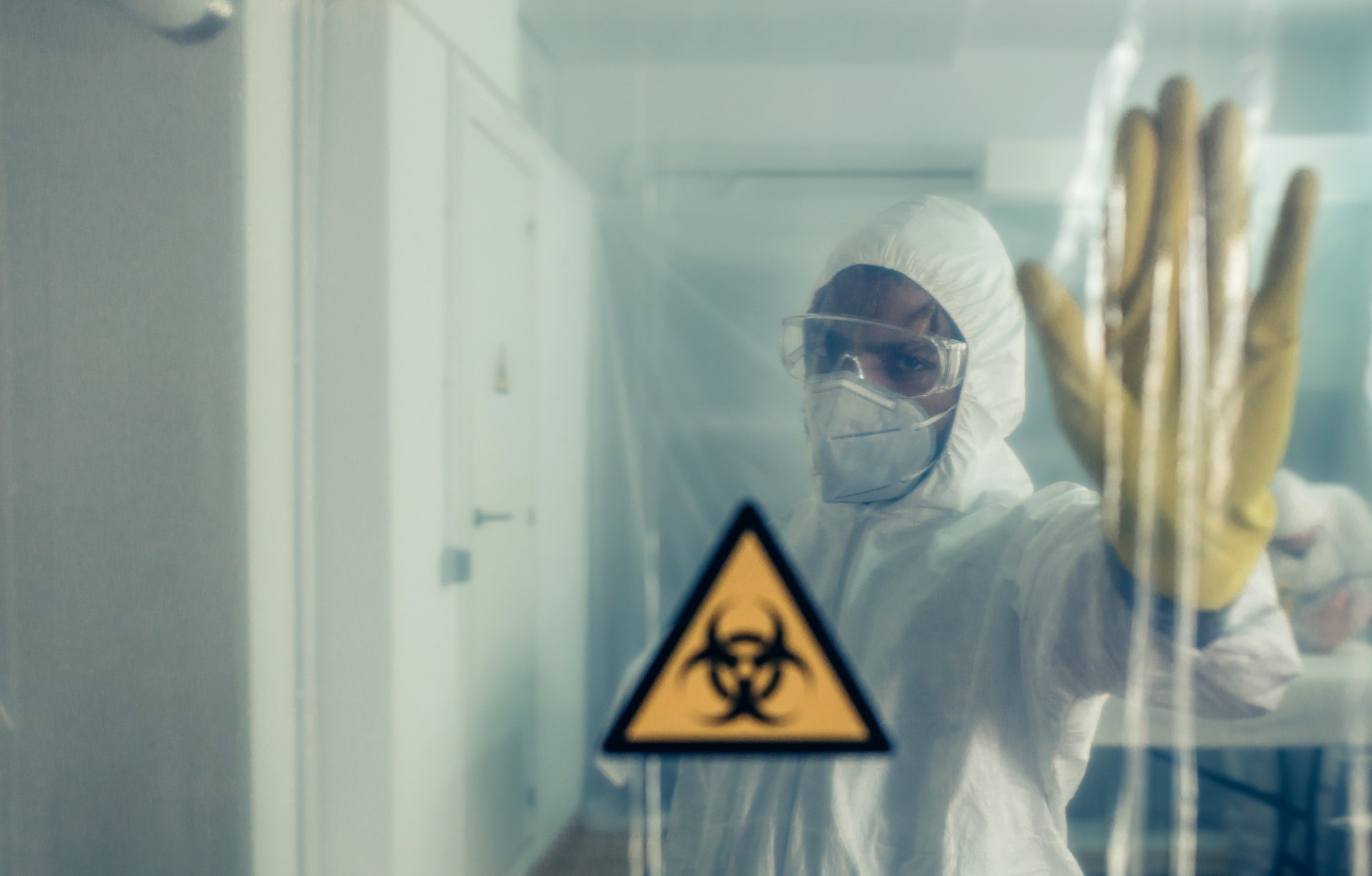 Scientist in hazmat suit in sealed-off area with biohazard sign