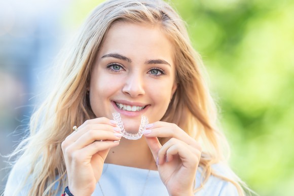Woman smiling while holding clear teeth aligner. 