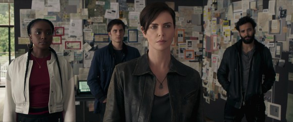Two woman and two men standing in front of walls papered with newspaper clippings and other documents. 