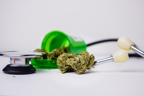 Cannabis flower spilling from a pill bottle next to a stethoscope. 
