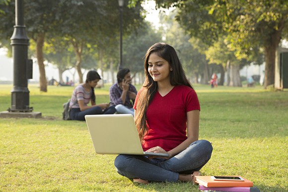 A young woman sitting on the ground uses her laptop.