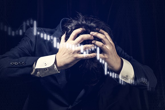 Man holding his head in panic behind falling stock chart.