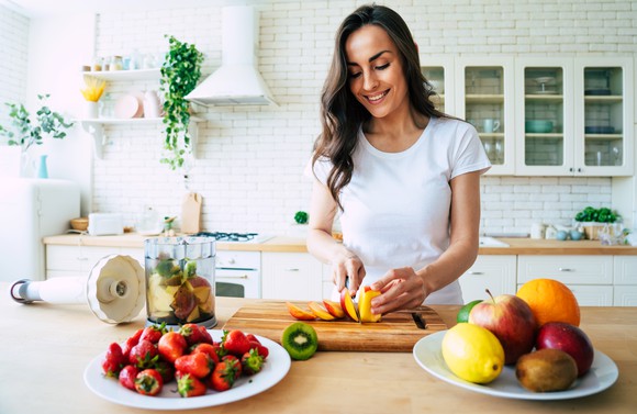 Woman in a kitchen cutting fruits to make smoothie.