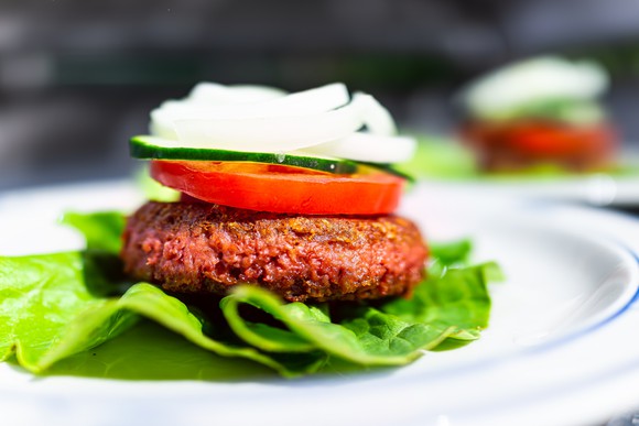 A plant-based burger patty on a bed of lettuce with a tomato and onion on top. 
