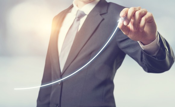 A person in a business suit is drawing an upwardly sloping line.