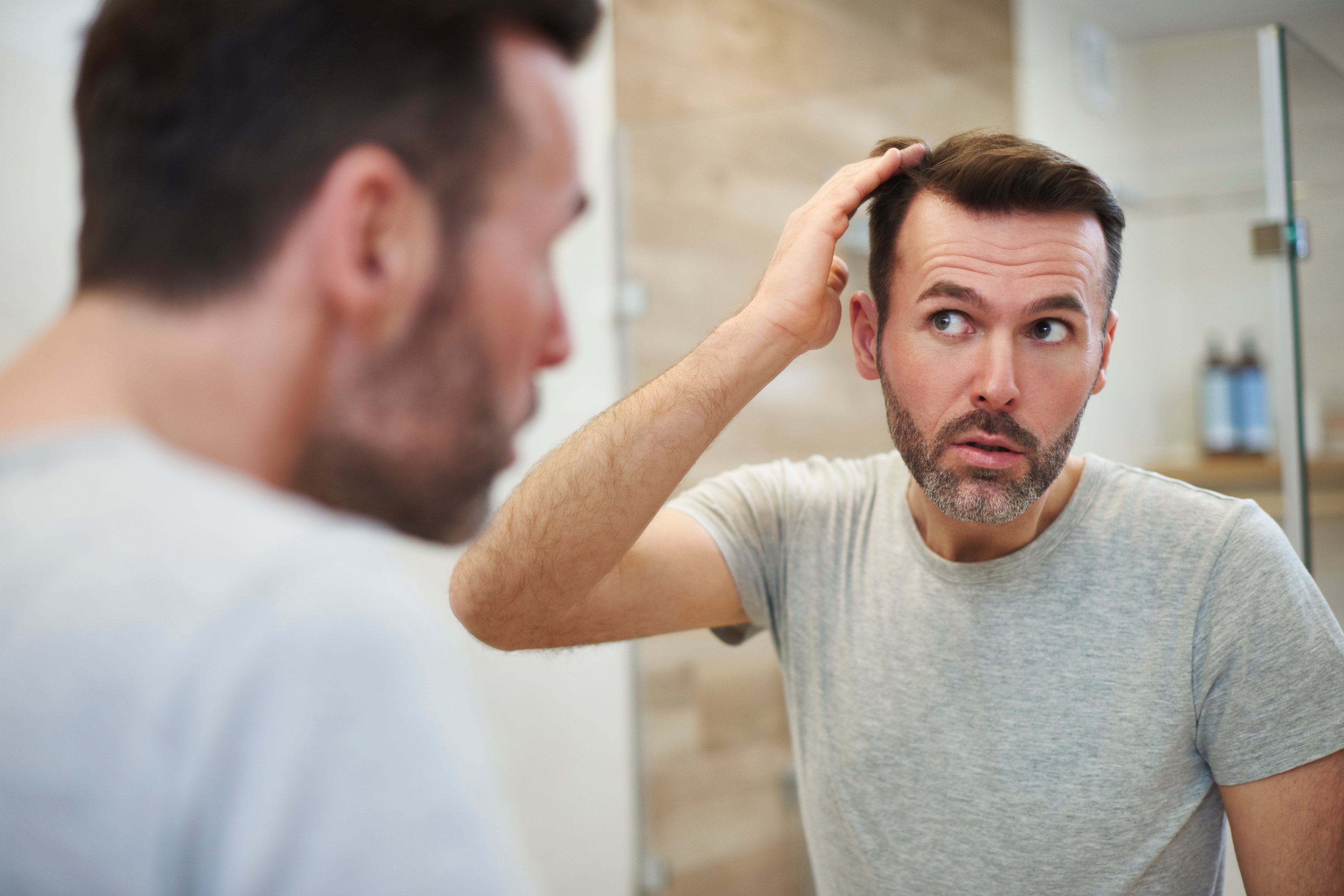 A man checks his hair in the mirror. 