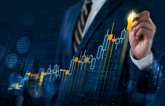 A person wearing a business suit is pointing at an upward sloping digital stock chart. 