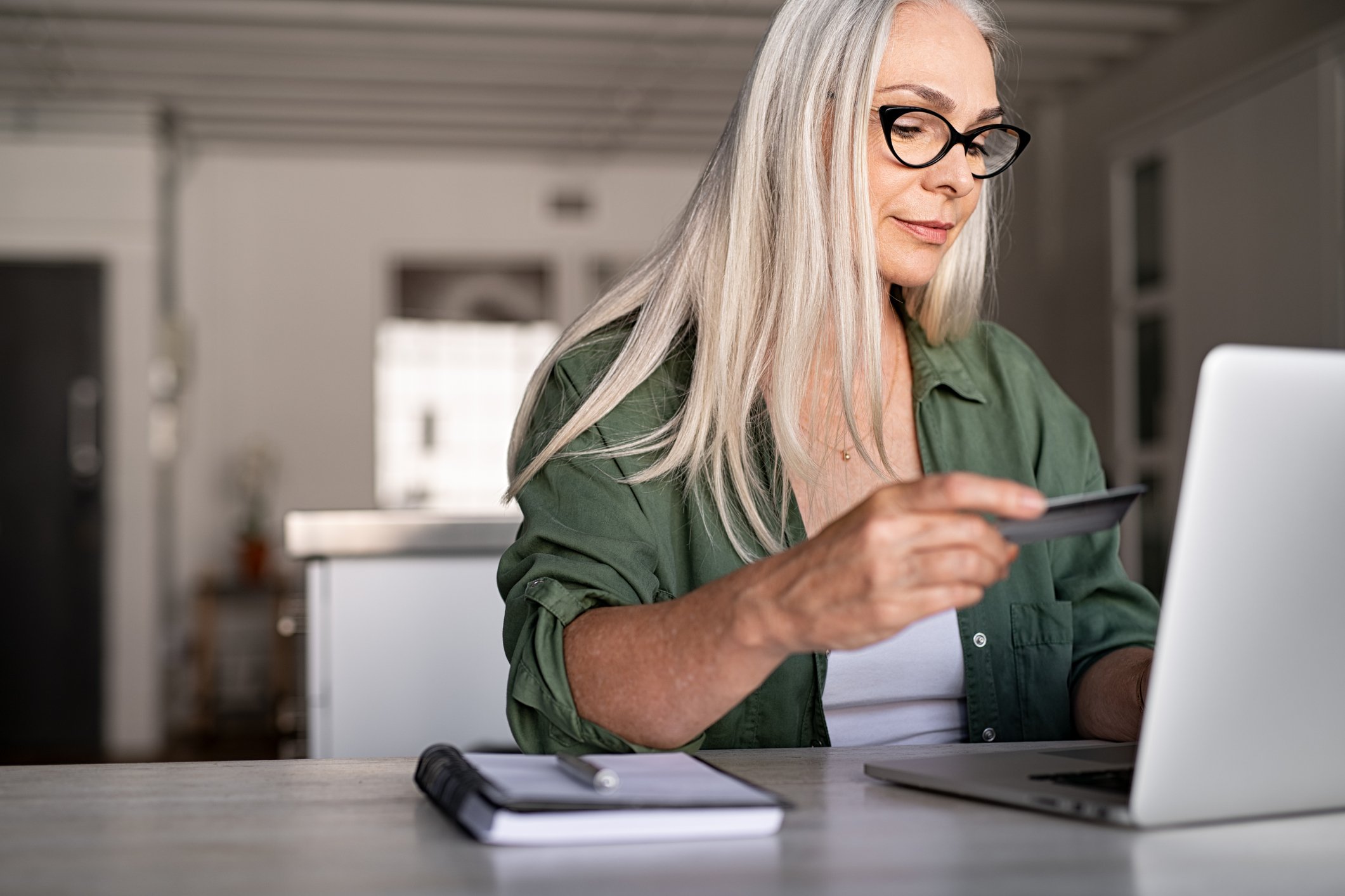 A woman looking at credit card while typing on laptop. 
