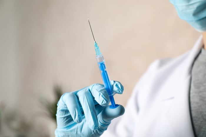 A researcher holds up a vaccine dose in a gloved hand.