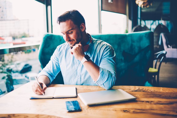 Man taking notes at wooden table.