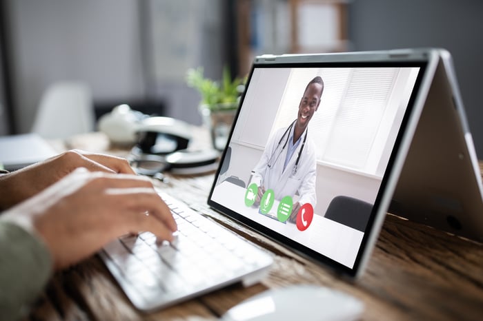 A person at a laptop displaying a doctor in a telehealth consultation