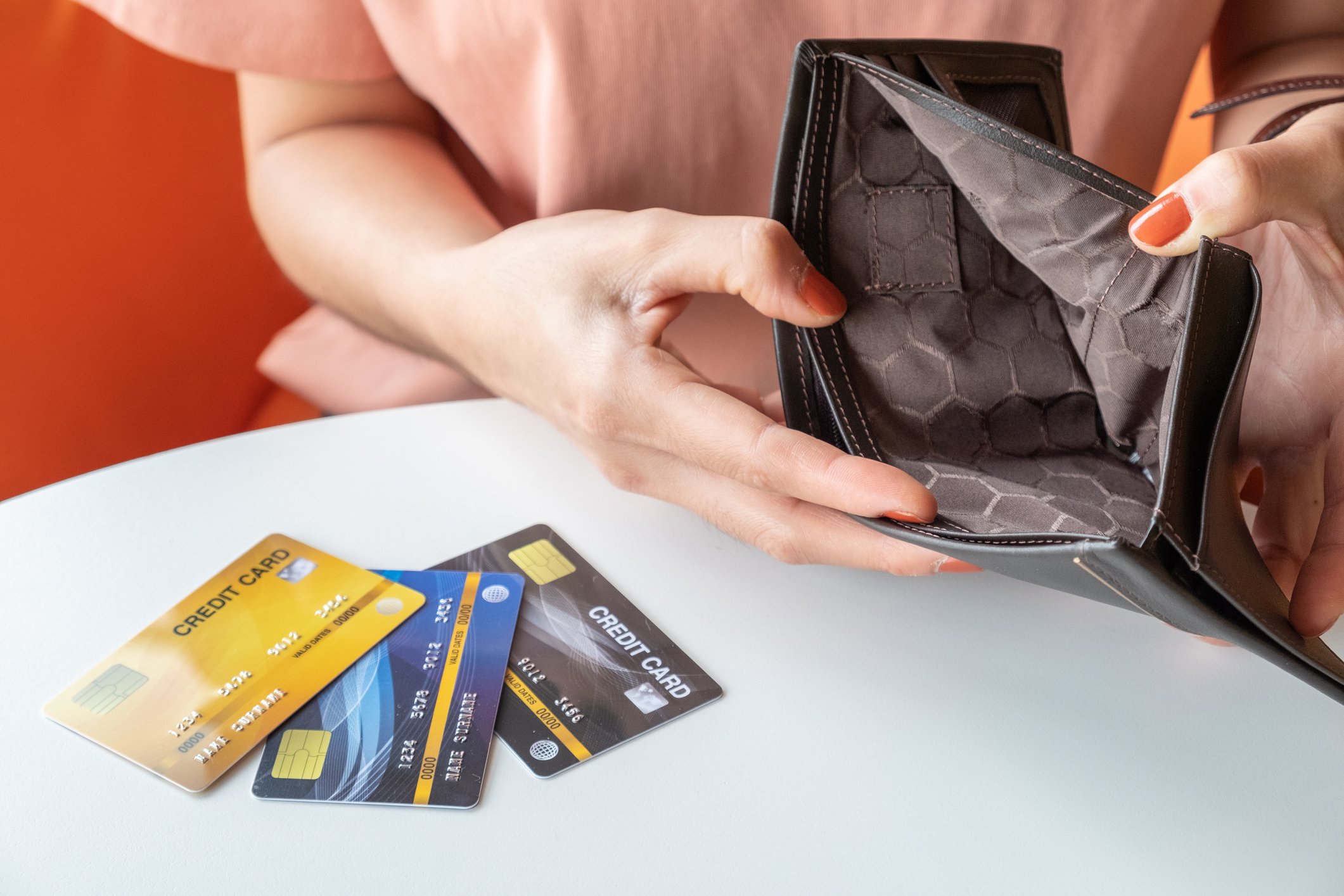 Woman holding an empty wallet, with credit cards on table
