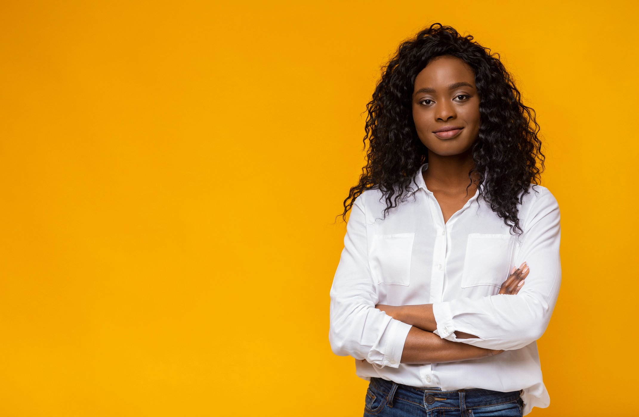 A woman standing in front of a yellow screen with her arms crossed, smiling. 