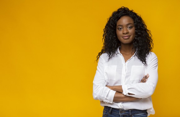 A woman standing in front of a yellow screen with her arms crossed, smiling. 